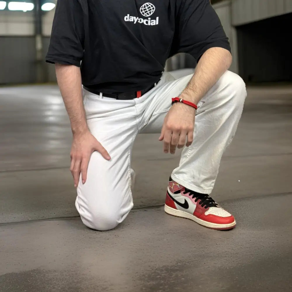 Man kneeling in white pants wearing red sneakers with a black leather belt featuring a red accent and metal buckle