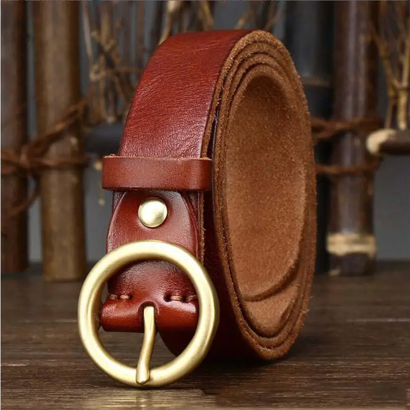 Hasti Belt Women’s Leather Belt with Brass Circular Buckle on rolled brown leather surface