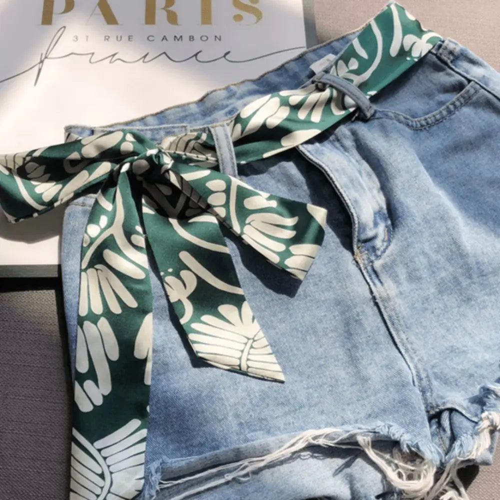 Denim shorts styled with a green and white patterned scarf belt for a fashionable look