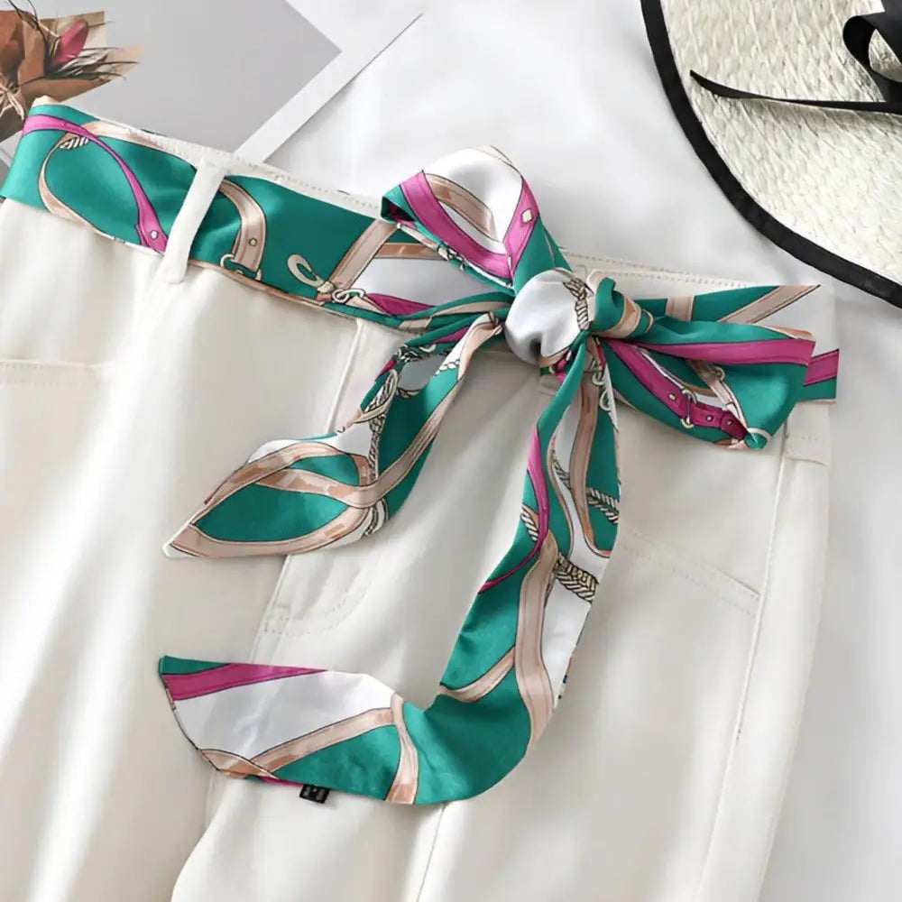 White pants with Betina scarf belt featuring a green, pink, and white patterned scarf