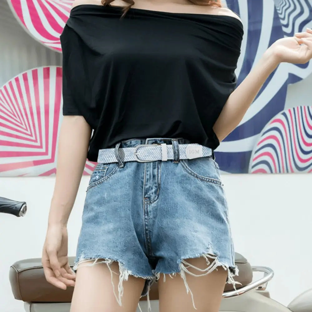 Woman wearing off-the-shoulder black top and denim shorts with woven pastel belt