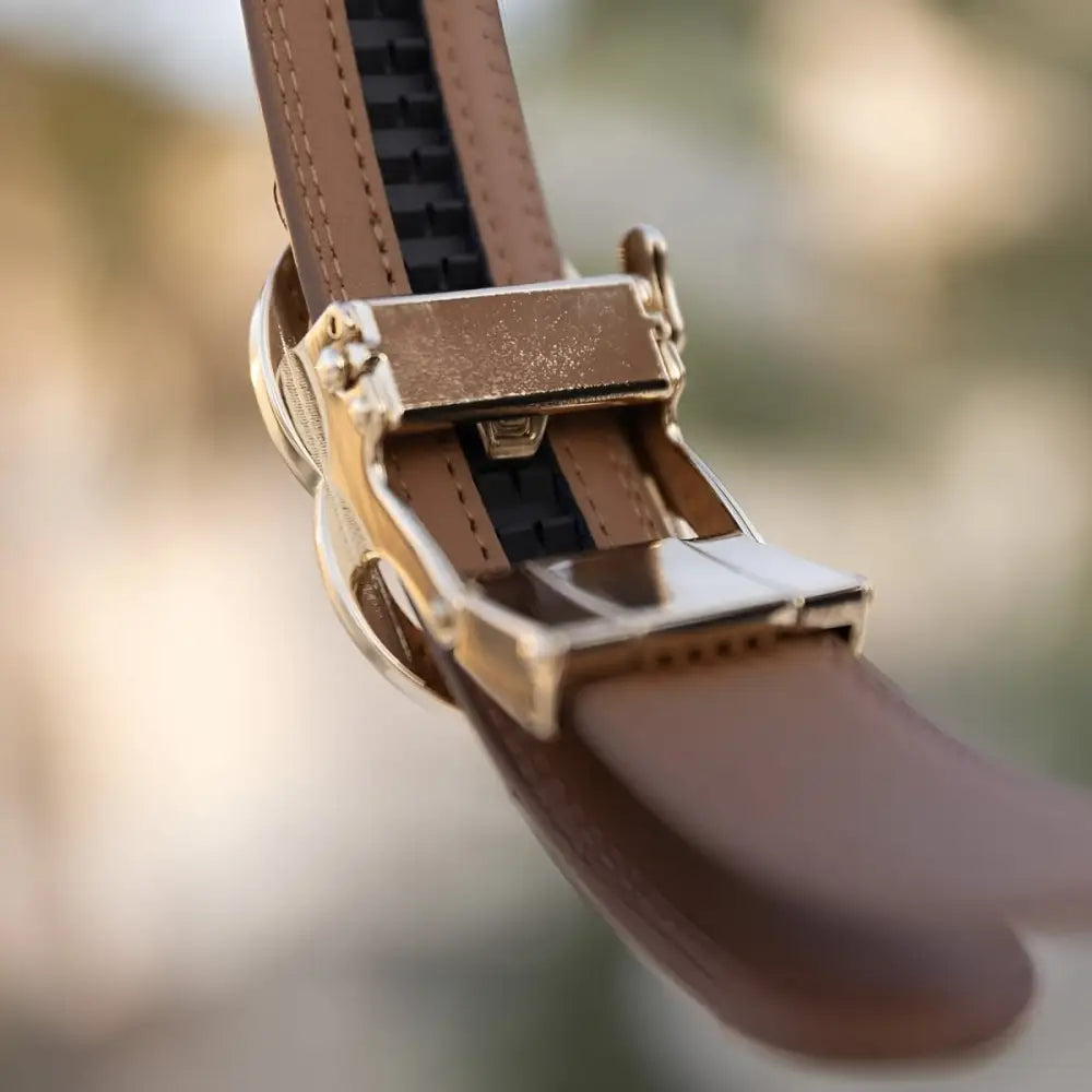 Brown leather ratchet belt with gold buckle worn by woman in black tank top and white pants